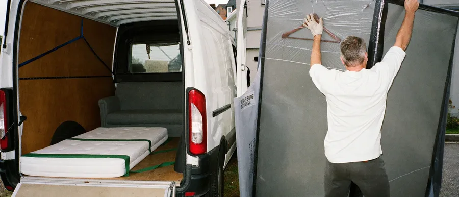 Zwei Helfer verladen ein in Decken verpacktes Möbelstück in einen Transporter